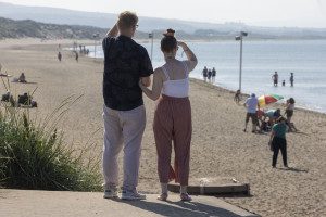 Brian and Claire are standing arm in arm with their backs to the camera, looking out at a beach