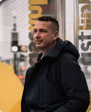 A man standing outside, smiling slightly