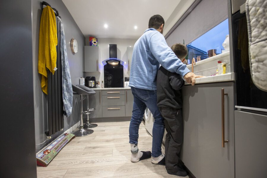 Father, with an electronic monitoring device on his ankle, in the kitchen with his son.
