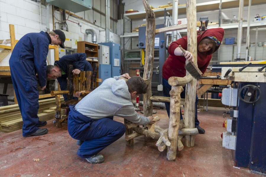 A workshop: a small group of people working together to build a chair made from driftwood